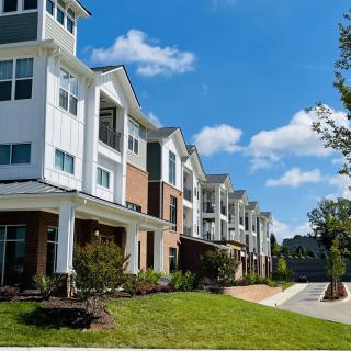 A row of modern suburban apartment buildings with a well-maintained lawn and a clear blue sky.