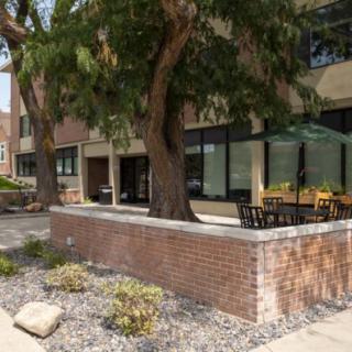An outdoor patio with tables and chairs, surrounded by a brick wall and trees along a sidewalk.