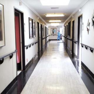 A hospital corridor with rooms on either side, featuring bright lighting and clean floors.