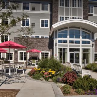 A building with outdoor seating and umbrellas, surrounded by landscaped gardens and flowers near the entrance.