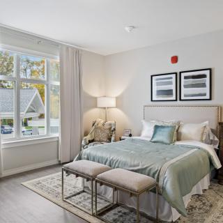 A cozy and modern bedroom with a large window, featuring a neatly made bed, bedside lamps, and elegant decor.