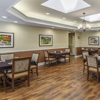 A well-lit dining room with wooden flooring and neatly arranged tables and chairs.