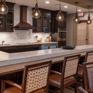 A modern kitchen with dark wood cabinets, pendant lighting, and a long countertop featuring bar stools.