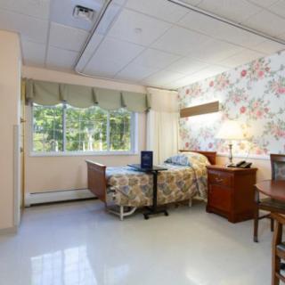 A cozy hospital room with a single bed, wooden furniture, and a floral wallpaper design.