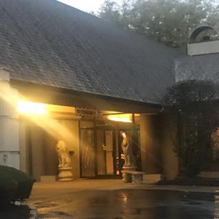 A tranquil evening view of a building entrance illuminated by warm light, featuring decorative statues on either side.