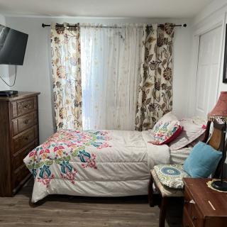 A cozy bedroom with a single bed featuring floral bedding, a wooden dresser, and a wall-mounted television.