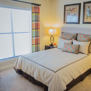 A cozy and well-decorated bedroom with a neatly made bed, bedside lamp, and framed artwork on the walls.