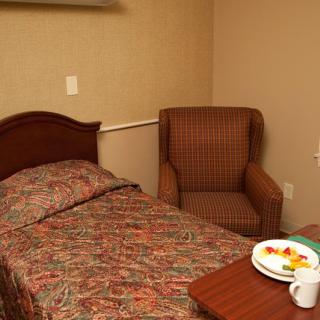 A cozy bedroom with a single bed, armchair, and a small table holding a plate of food and a mug.