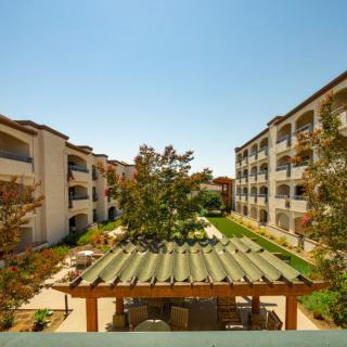 A view of apartment buildings surrounding a landscaped courtyard with an outdoor patio on a sunny day.