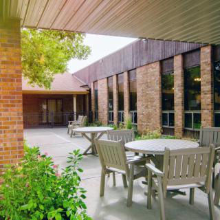 An outdoor patio area with tables and chairs adjacent to a brick building.