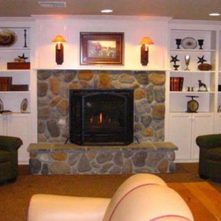 A cozy living room featuring a stone fireplace and surrounding shelves with decor.