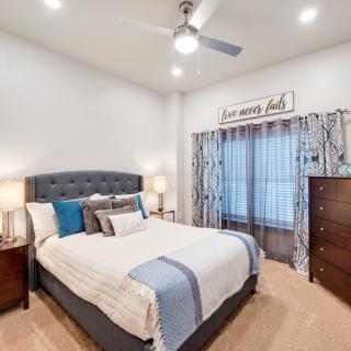 A modern bedroom with stylish decor, featuring a bed with decorative pillows, bedside lamps, and a ceiling fan.