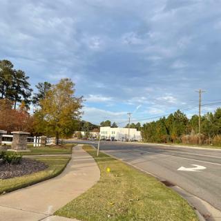 A suburban intersection with a sidewalk surrounded by trees under a cloudy sky.
