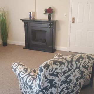 A cozy living room featuring a decorative black fireplace, an ornate patterned chair, and accent decor including a vase with flowers.