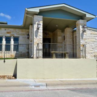 A stone house with a porch and railing in a residential area under a clear blue sky.