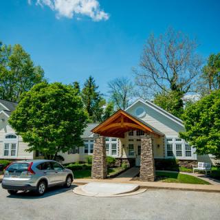 A picturesque house with a welcoming entrance, surrounded by lush greenery and parked car under a clear blue sky.