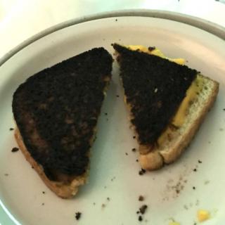 A burnt grilled cheese sandwich cut into halves on a plate.