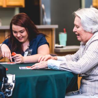 A caregiver and an elderly woman enjoying a card game together, fostering connection and joy.