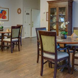 A cozy dining room with wooden tables and chairs, featuring a cabinet and decorative orchids.