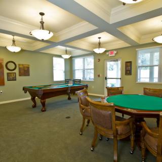 A well-appointed game room featuring a pool table and a card table with chairs, illuminated by ceiling lights.