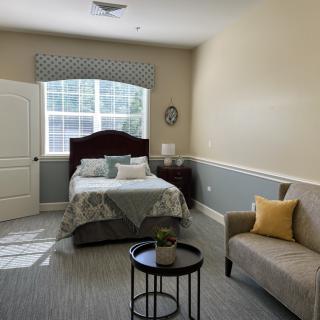 A cozy bedroom with a bed, sofa, and natural lighting from a large window.