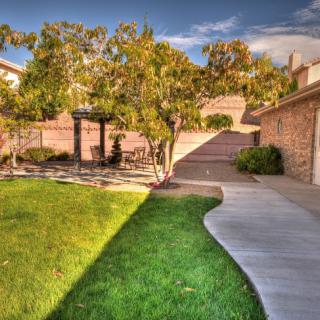 A beautifully landscaped backyard featuring a lush green lawn, a winding pathway, and mature trees under a clear sky.