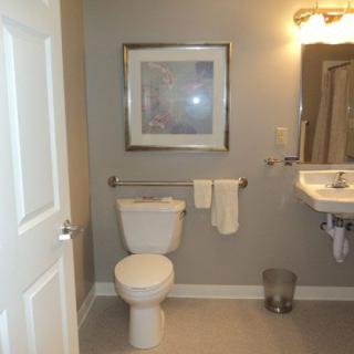 A clean bathroom with a toilet, sink, and mirror, featuring a framed picture and bright lighting.