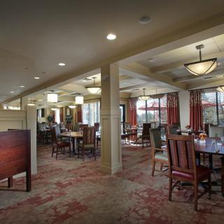 A cozy dining room with elegant tables and chairs, featuring warm lighting and a patterned carpet.