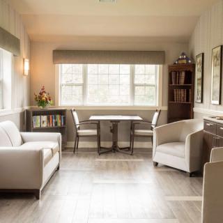 A cozy and inviting living room with neutral tones, featuring a sofa, chairs, table, and a bookshelf by the window.