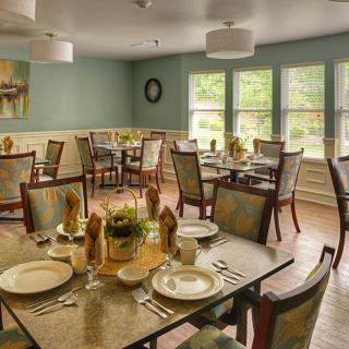 An elegantly set dining room with multiple tables and chairs, featuring natural light from large windows.