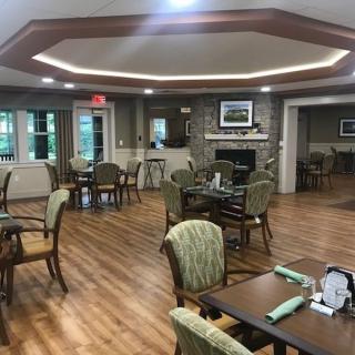 A cozy dining area with wooden floors, neatly arranged tables and chairs, and a stone fireplace.