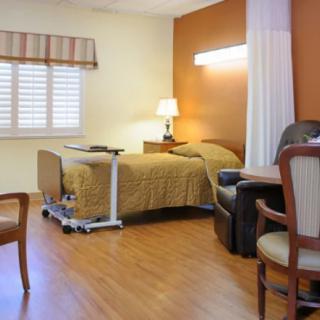 A tidy and well-lit hospital room with a single bed and seating area.