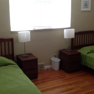 A bedroom with two twin beds featuring green bedding, accompanied by nightstands and lamps, with a window above.