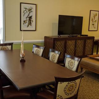 A cozy dining room featuring a wooden dining table with chairs, a television on a cabinet, and decorative artwork on the walls.