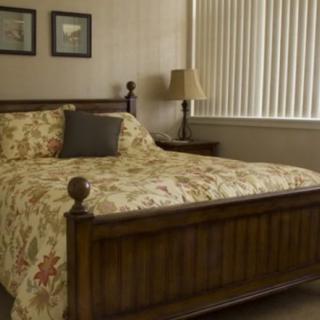 A cozy bedroom with a floral-patterned bedspread, wooden bed frame, and a bedside lamp.