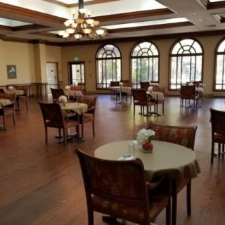 An empty dining room with neatly arranged tables and chairs, featuring large windows and elegant lighting.