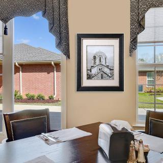 A dining room with a table set near large windows, featuring a framed artwork on the wall.