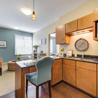 A cozy studio apartment featuring a compact kitchen with wood cabinets and an open living and dining area.