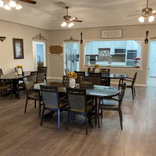 A cozy dining area with multiple tables and chairs, featuring a view into the kitchen and lit by ceiling fans.