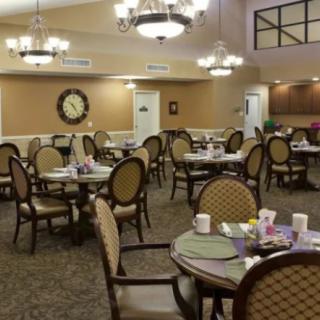 A well-lit dining area with round tables and elegant chairs, featuring chandeliers overhead.