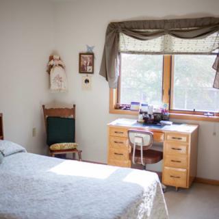 A cozy bedroom featuring a bed, desk, and window with natural light.