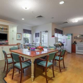 A well-lit dining and kitchen area with a large wooden table, surrounded by chairs, and modern kitchen appliances in the background.