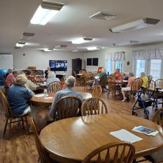 A lively gathering at a community center, where people are engaged in conversation and watching a program on television.