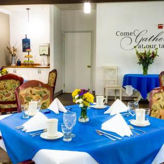 A beautifully set dining area with blue tablecloths and floral centerpieces.