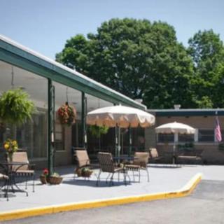 A motel patio area with outdoor seating and umbrellas, surrounded by greenery.