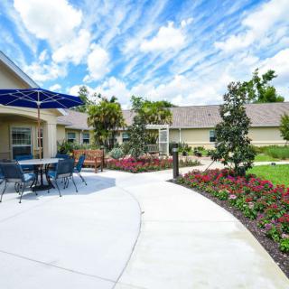A well-maintained garden with a patio area, featuring outdoor furniture and colorful flowerbeds under a bright blue sky.