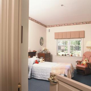 A cozy bedroom with a bed, dresser, and armchair near the window.