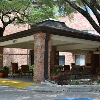 A building entrance with a canopy, surrounded by trees and outdoor seating.