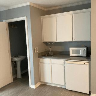A compact kitchenette with white cabinets, a sink, microwave, and mini refrigerator in an apartment.
