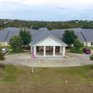 Aerial view of a large building with a prominent front entrance and columns, featuring a flagpole in the foreground.
